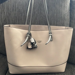 Dimm-rosa axelväska från Guess -  Dimm-rosa axelväska från Guess med fina detaljer och dubbla handtag. Väskan har en praktisk ficka på baksidan och ett rymligt inre med mönstrat foder. Original pris 600 kr, men lite slitna blommor därav det låga nuvarande priset. 