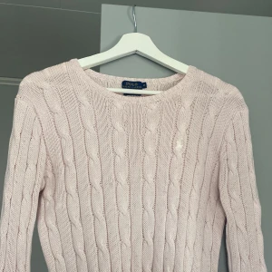 Ljusrosa Polo Ralph Lauren tröja stickad - Säljer en ljusrosa stickad tröja från Polo Ralph Lauren i pima bomull. Tröjan har ett klassiskt flätmönster och rund halsringning. Perfekt för en stilren och bekväm look. Storlek M men sitter som S