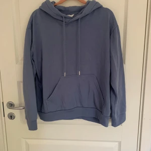Blå hoodie från H&M - Säljer en bekväm blå hoodie från H&M. Den har en klassisk känguruficka och justerbar huva med snören. Perfekt för en avslappnad stil. Passar bra till jeans eller mjukisbyxor. Inga defekter men använd ett fåtal gånger.