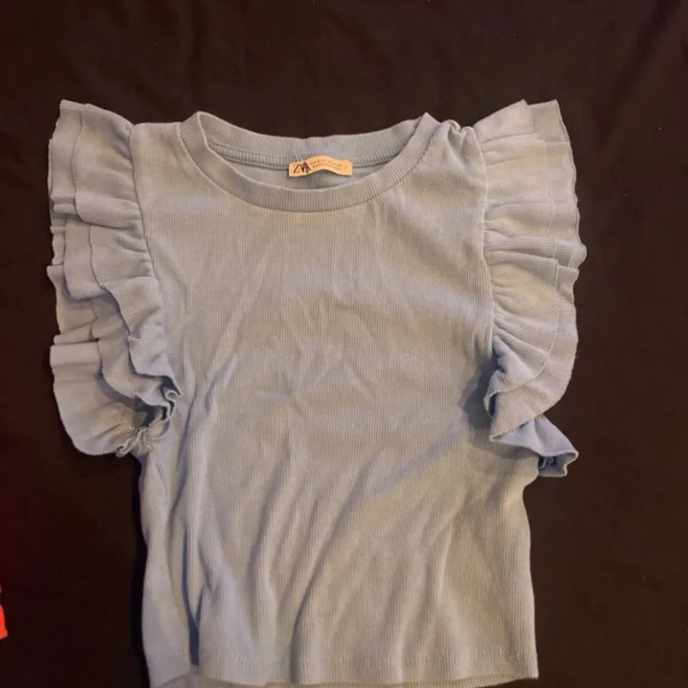 Säljer en söt ljusblå ribbad topp från Zara med volangdetaljer på ärmarna. Perfekt för en stilren och trendig look. Toppen har en rund halsringning och korta ärmar.. Yläosat.