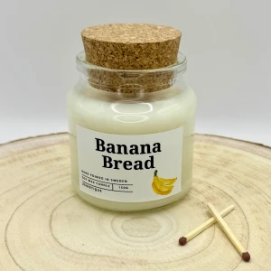 Doftljus Banana Bread 150g - Doftljuset med doften Banana Bread har en härligt varm och inbjudande doft där söt, mogen banan står i fokus. Den lena och naturliga banandoften kompletteras av en mjuk bakverksarom med en hint av vanilj och kryddor. En mysig och tröstande doft som påminner om nybakat bananbröd direkt från ugnen.  Egenskaper:  - Brinntid: ca 30-35 timmar - Vax: 100 % sojavax - Veke: Vaxad bomullsveke - Behållare: Glas, kan tvättas ur och återanvändas - Netto vikt: 150g