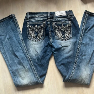 Miss Me jeans - Snygga blå jeans från Miss Me med unika broderade fickor bak. Jeansen har en klassisk femficksdesign och är dekorerade med silverfärgade knappar och detaljer. Perfekta för dig som vill ha något extra i garderoben! De är en stor 28 som storlek. Midjemått tvärs över 42cm.  inner benlängd 93cm 