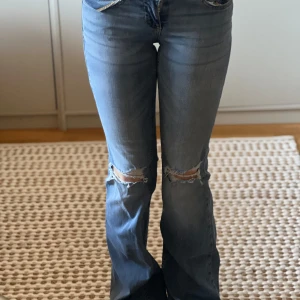 Blå bootcut jeans från Nelly - Snygga blå bootcut jeans från Nelly med slitna detaljer på knäna. De har en klassisk femficksdesign och är tillverkade i ett bekvämt denimtyg. Perfekta för en avslappnad stil. Storlek 32. Används ungefär 4-5 ggr så är i mycket bra skick 