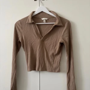 Beige ribbad tröja från H&M - Säljer en stilren beige ribbad tröja från H&M. Tröjan har en v-ringad krage och långa ärmar, perfekt för en avslappnad look. Den är croppad och passar bra till både jeans och kjol. Perfekt för höst och vår!