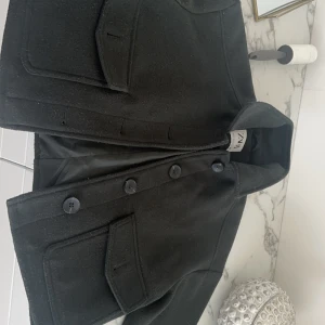 Grön kappa med knappar - Snygg grön jacka från Zara  med stora knappar framtill. Jackan har en klassisk design med två fickor och en stilren krage. Perfekt för kyligare dagar. OBS!  (Den är nopprig i tyget men har inga specifika defekter som påverkar helhetsintrycket!) 