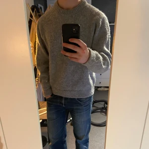 Grå stickad tröja - Säljer en stilren grå stickad tröja med rund halsringning. Tröjan har långa ärmar och en bekväm passform, perfekt för kyligare dagar. Passar bra till jeans eller andra casual outfits.