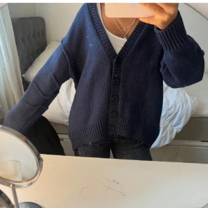 Mörkblå kofta från Zara - Säljer en mysig mörkblå kofta från Zara med knappar framtill. Koftan har en djup v-ringning och ribbade muddar vid ärmslut och nederkant. Perfekt för en avslappnad stil.