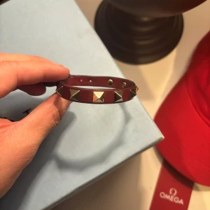 Valentino Armband - Snyggt Vinrött valentino armband med guldiga spikar. Storlek är one size få passar de flesta! sparsamt använt så Mycket fint skick. Modellen är Unisex, Nypris på dessa ligger på cirka 3000kr. Inga tillbehör till armbandet endast armbandet