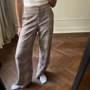 Rutig byxa från KappAhl - Snygga rutiga byxor från KappAhl i en mix av beige, brun och blå. Byxorna har en högmidjad passform och vida ben, vilket ger en trendig look. Perfekta för att ge din outfit en stilfull touch.