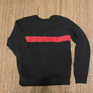 Svart tröja Woolrich - Säljer denna svarta tröjan från Woolrich med röd text. Denna är i bra skick men lite urtvättad. Köpt från Plick för 600kr men sitter för stor för mig. Kom privat för fler frågor!