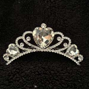 Glittrig diadem tiara med hjärtformade stenar - Elegant diadem tiara med stora hjärtformade stenar och glittrande detaljer. Perfekt för att ge en touch av glamour till din look. Tiara har en kam för att enkelt fästa i håret.