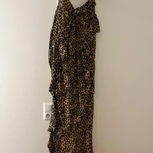 Leopardmönstrad klänning med volang - Snygg leopardmönstrad klänning med volangdetaljer. Perfekt för en djärv och trendig look. Klänningen har en elegant och flytande design som ger en feminin touch.