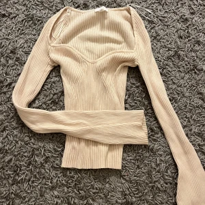 Beige ribbad topp från H&M - Säljer en stilren beige ribbad topp från H&M. Toppen har långa ärmar och en elegant passform som framhäver figuren. Perfekt för en chic och avslappnad look. 
