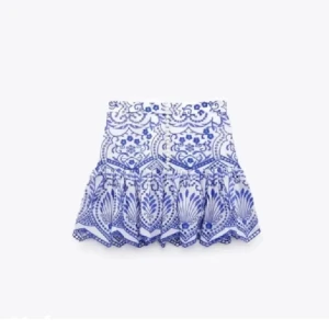 Vit och blå kjol från Zara - Snygg vit och blå kjol från Zara med ett vackert blommönster. Kjolen har knappar framtill och en volangdetalj vid fållen. Perfekt för en somrig look!