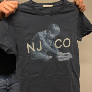 Mörkblå t-shirt med tryck - Säljer en mörkblå t-shirt med ett coolt tryck av ett barn som leker. T-shirten har korta ärmar och rund halsringning. Perfekt för en avslappnad stil.