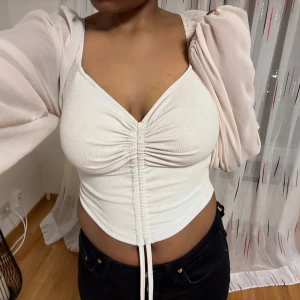 Beige korsettopp med långa ärmar - Säljer en snygg beige korsettopp från shein med långa, transparenta ärmar och snörning framtill. Toppen går att ändra till en magtröja. Perfekt med vita eller svarta jeans. 