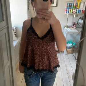 Leopardmönstrad linne med spetsdetaljer - Säljer en snygg leopardmönstrad linne med svarta spetsdetaljer vid halsringning och nederkant. Linnet har smala axelband och en lös passform, perfekt för en trendig look. använt 1 gång💞😊
