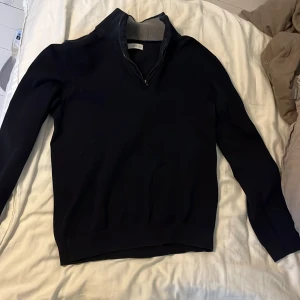 Svart tröja med dragkedja från MNG - Säljer en stilren svart tröja från MNG med dragkedja vid halsen. Perfekt för en avslappnad look. Tröjan har långa ärmar och en ribbad krage i grått.