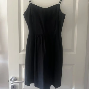 Svart klänning med smala axelband - Säljer en elegant svart klänning med smala axelband och rynkad detalj på ryggen. Perfekt för en stilren look. Klänningen har en klassisk design som passar många tillfällen.