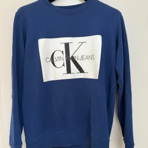 Blå Calvin Klein sweatshirt M - Blå sweatshirt från Calvin Klein Jeans med stor vit logga framtill. Den är mycket sparsamt använd och är därför i väldigt bra skick! 