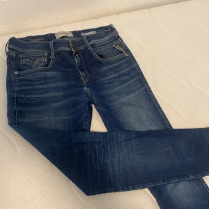 Replay Hyperflex blå jeans, W29 L34 - Snygga Replay Hyperflex jeans i klassisk blå tvätt med coola slitningar och kontrastsömmar. Modellen har fem fickor, läderpatch bak och smal passform som sitter riktigt schysst. Perfekta stretchjeans för dig som vill ha både stil och komfort.