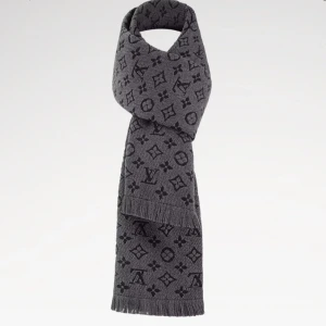 Grå Louis Vuitton halsduk i ull - Snygg grå halsduk från Louis Vuitton med ikoniskt monogrammönster i mörkare grå toner. Halsduken är i 100% ull och har fransade kanter för en extra cool vibe. Perfekt accessoar för att lyfta din vinterstil.