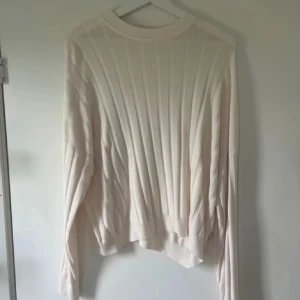 Ribbad vit stickad tröja - Säljer en ribbad vit stickad tröja med lång ärm och relaxed fit. Tröjan har en rund halsringning och är perfekt för lager-på-lager. Enkel och stilren design som passar till många olika outfits.