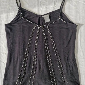 Svart linne med silverpärlor Lindex - Coolt linne med smala axelband från Lindex ❤️  Utsmyckad med silverfärgade pärlor. Storlek XS på lappen men egentligen större, passar mig som har S-M. Ett par pärlor saknas framtill och finns trådar som behöver fästas, se bilder. I övrigt i fint skick!  Hör gärna av er vid frågor och glöm inte att kolla in garderoben för fler liknande plagg, bundlerabatt finns! 💕