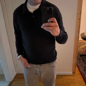 Svart pikétröja från Selected Homme - Säljer en svart pikétröja från Selected Homme i storlek L. Tröjan har klassisk krage och knäppning framtill, lång ärm och är tillverkad i mjukt material som känns skönt mot huden. Perfekt för en stilren och enkel look.