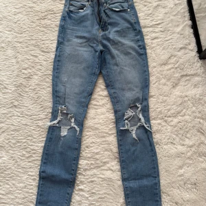 Blå skinny jeans med slitna knän - Säljer ett par blå skinny jeans med rejält slitna och trasiga knän. Jeansen har klassisk femficksdesign och är i stretchigt denim som sitter tight hela vägen ner. Perfekta för dig som gillar en edgy och avslappnad stil.