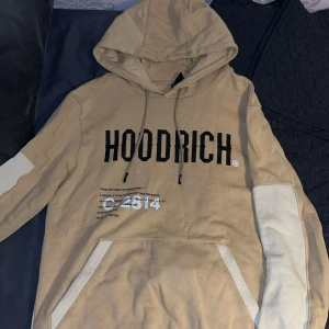 Beige hoodie från Hoodrich XS - Säljer en beige hoodie från Hoodrich i storlek XS. Tröjan har kontrastpaneler i vitt på ärmar och nederkant, stor svart logga framtill och världskarta med tryck på ryggen. Utrustad med huva och känguruficka. Perfekt för en chill streetwear-look.