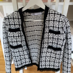 Rutig cardigan jacka från Zara S - Snygg svartvit rutig cardigan jacka från Zara i storlek S. Jackan har stickad känsla, dekorativa fickor och svarta kanter. Perfekt för dig som gillar klassisk men trendig stil. Långärmad och med coola detaljer nertill.