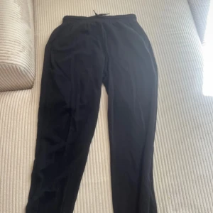 Svarta mjukisbyxor från H&M Divided - Svarta mjukisbyxor från H&M Divided i storlek S. Byxorna har resår i midjan med snörning och muddar vid bensluten. Tillverkade i mjukt bomullsmaterial med inslag av polyester, perfekta för chill eller träning.