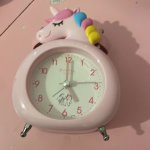 Söt enhörningsväckarklocka rosa - En gullig väckarklocka i form av en enhörning med rosa, blå och gula detaljer. Klockan är ljusrosa med enhörningsmotiv både på toppen och på urtavlan. Perfekt för dig som älskar magiska och färgglada prylar till rummet.