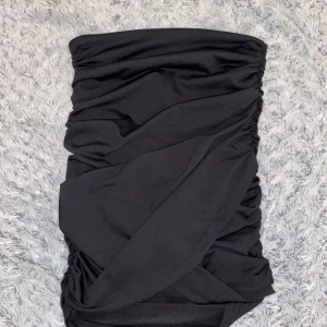 Svart omlottkjol med rynkade detaljer - Snygg svart kortkjol med omlott-design och rynkade sidor. Kjolen är inte använd en ändå gång💘 kjolen är medel hög i midjan och går inte riktigt hela vägen ner till knäna