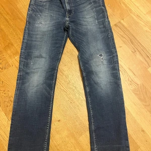 Blå jeans med slitningar - Snygga blå jeans med coola slitningar och tvättade detaljer på både fram- och baksida. Klassisk femficksmodell med raka ben och normal passform. Perfekta för dig som gillar en avslappnad streetstil. Materialet är robust denim som håller länge.