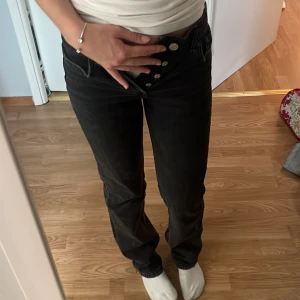 Svarta straight jeans från Zara - Säljer ett par svarta jeans från Zara i storlek 34. Modellen har rak passform och klassisk femficksdesign med knappgylf. Jeansen är midwaist och tillverkade i jeansmaterial med en mörk tvätt. Perfekta för dig som gillar en clean och enkel look.
