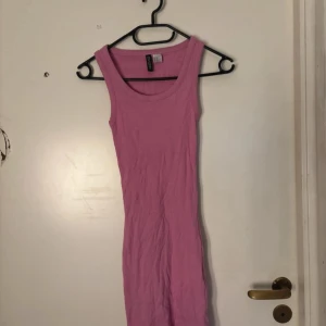 Rosa ärmlös kortklänning H&M - En enkel och snygg rosa kortklänning från H&M. Klänningen är ärmlös med rund halsringning och har en tight passform. Perfekt för varma dagar eller att styla med en jacka. Tillverkad i mjuk bomull för skön känsla.
