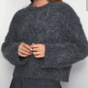 Grå fluffig stickad tröja Wakakuu - Supermjuk och fluffig grå stickad tröja från Wakakuu Icons. Tröjan har en croppad passform, rund hals och långa ärmar. Perfekt för lager-på-lager och ger en cool, avslappnad vibe till din outfit. Nypris är 2500 kr men priset kan diskuteras.