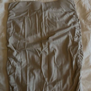 Beige lång tight kjol  - Säljer en beige tight kjol från Gina Tricot i storlek XXS. Kjolen är lång och har snygga rynkade detaljer längs sidorna. Materialet känns mjukt och stretchigt.