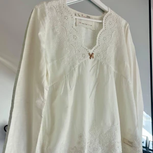 Vit Odd Molly blus med spetsdetaljer - Supersöt vit blus från Odd Molly med broderade spetsdetaljer och v-ringning. Långärmad modell med liten rosett framtill och vackert mönstrad kant runt halsen. Storlek 2, skulle säga M. Aldrig använd, hängd i garderob.
