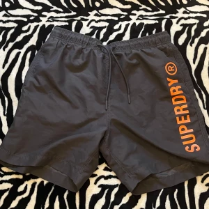 Grå Superdry shorts med snörning - Snygga grå shorts från Superdry med orange logga längs benet🍒🖤funkar också som bad shorts🍒🖤