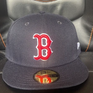 Boston Red Sox keps New Era 59FIFTY - Snygg Boston Red Sox keps från New Era 59FIFTY med klassisk röd B-logga framtill. Kepsen är svart med platt skärm och officiell MLB Authentic Collection-märkning. Perfekt för dig som vill ha sportig stil och visa ditt lag.