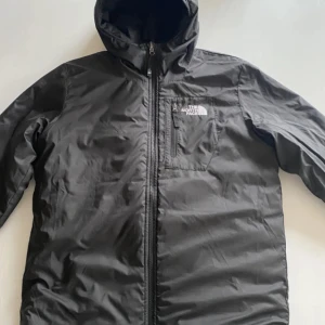Svart quiltad pufferjacka The North Face - Säljer en svart pufferjacka från The North Face med huva och dragkedja framtill. Jackan är quiltad och har en bröstficka med logga. Perfekt för kyliga dagar och har en clean, sportig look. Säljs billigare pga hålet bredvid högra fickan 