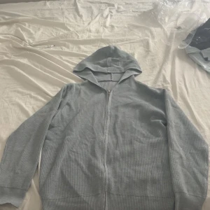 Grå stickad kofta  - Säljer en ljusgrå ribbad hoodie med dragkedja framtill och huva från axel luxe. Tröjan har långa ärmar och är tillverkad i ett mjukt, stickat material som känns skönt mot huden. Perfekt för en chill och avslappnad stil. Helt sprilansny aldrig använd. Pris kan gå ner vid snabb affär😊