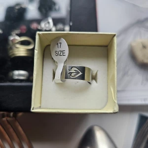 Bred silverfärgad ring med hjärtdetalj - Snygg och stilren ring i silverfärg med ett ingraverat hjärta på framsidan. Ringen är bred och har en modern, minimalistisk design. Storlek 17. Perfekt accessoar för att lyfta din look med en cool detalj. Rostfritt stål 17.3 mm