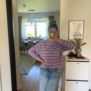  Randig långärmad tröja - S - Säljer en ljuslila långärmad tröja med svarta och vita ränder från ASOS i storlek S. Tröjan har en loose passform och är croppad i modellen, perfekt till jeans eller shorts. Mjuk bomullskänsla och rund hals.