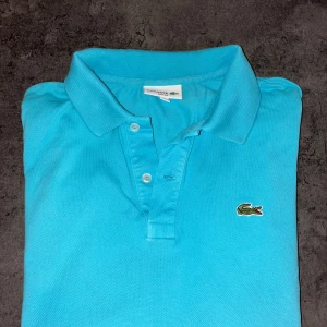 Turkos pikétröja från Lacoste  - Snygg turkos pikétröja från Lacoste i slim fit-modell. Storlek L. Skriv vid frågor eller funderingar.