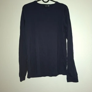 Mörkblå långärmad tröja BASIC U - Enkel och stilren mörkblå långärmad tröja från BASIC U. Tröjan har rund halsringning och är tillverkad i mjuk bomull, perfekt för lager-på-lager eller som den är. Passar dig som gillar en clean och klassisk look.