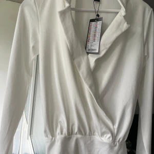 Vit omlottklänning från Amisu - Snygg vit omlottklänning från Amisu i storlek S. Klänningen har lång ärm, markerad midja och en stilren omlottdesign vid halsen. Perfekt för dig som gillar minimalistisk och fräsch stil. Materialet känns mjukt och har en lätt glansig finish.